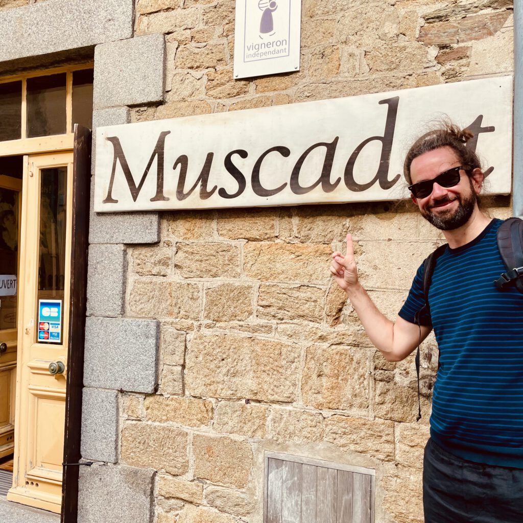 Ein (schöner) Mann zeigt auf ein "Muscadet"-Schild.