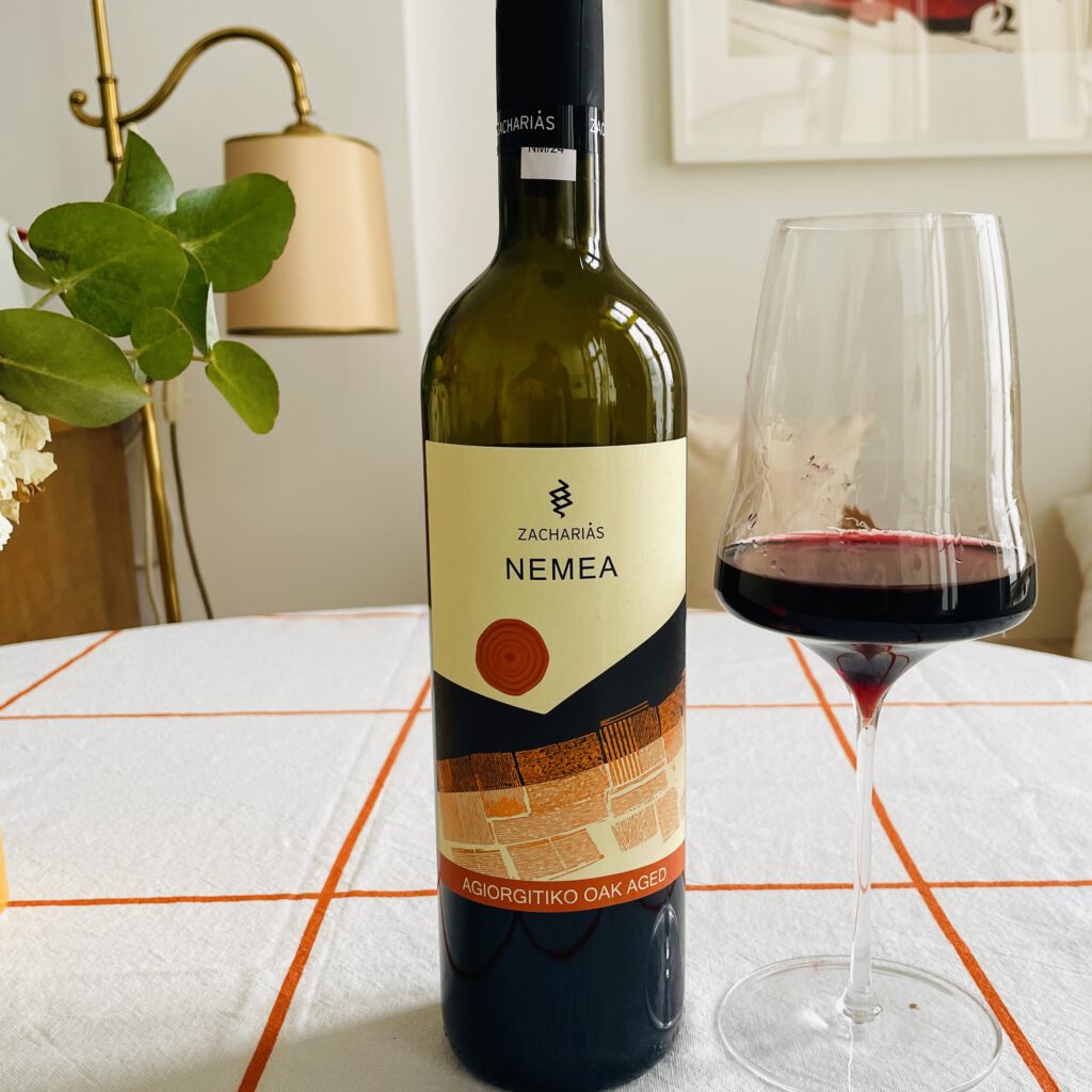 Eine Flasche Nemea vom Weingut Zacharias auf einem Tisch neben einem gefüllten Glas.