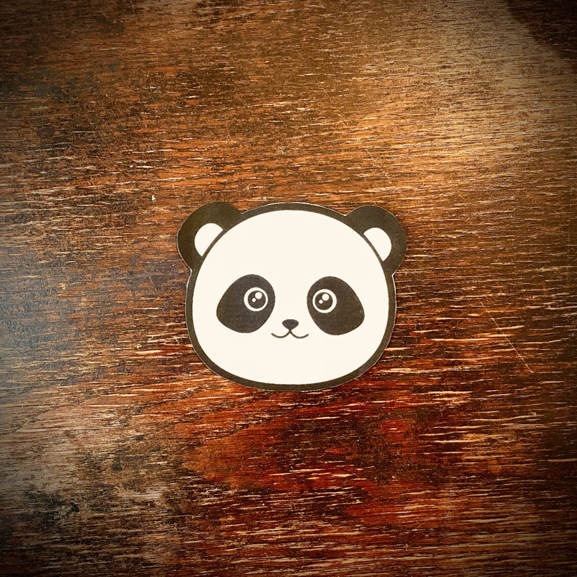 Ein stilisierter Panda-Kopf auf einem Holztisch.